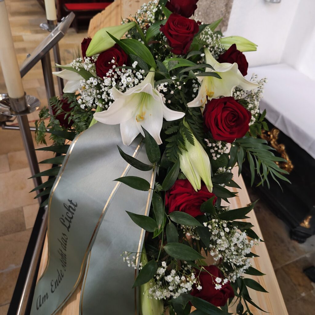 Sargschmuck mit Lilien und roten Rosen – Trauerblumen Vöcklabruck